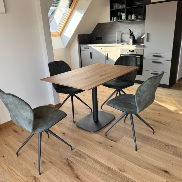 Elegante Stühle aus grauem Stoff um einen modernen Holztisch gruppiert, vor einer modernen Küchenzeile mit dunklen Akzenten.