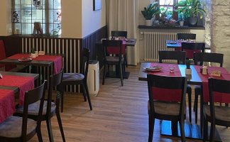 Ein gemütliches Restaurant mit roten Tischdecken und weißem Fußboden, beleuchtet von modernen hängenden Lampen.