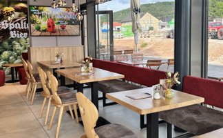 Die Inneneinrichtung des Cafés zeigt helle Holzmöbel, gemütliche Sitzgelegenheiten und eine große Fensterfront mit Ausblick.