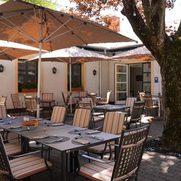 Gemütliche Terrasse mit eleganten Tischen und Stühlen, die auf einen sonnigen Tag in einem Restaurant hinweist.