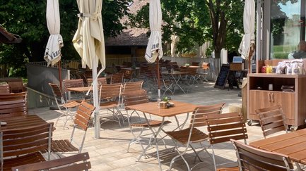 Sonnige Terrasse eines Restaurants, bestückt mit Tischen und Stühlen, bereit für Gäste, die das schöne Wetter genießen wollen.