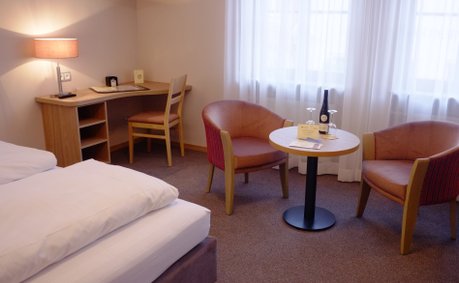 Der Raum kombiniert Komfort und Stil mit einem Doppelbett, einem Schreibtisch und einem einladenden Sitzbereich für Gäste.