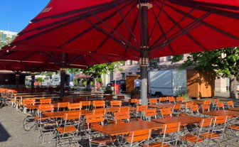 Weitläufige Freifläche mit Biergartentischen und -stühlen unter beschattenden Sonnenschirmen im Herzen von Ingolstadt.
