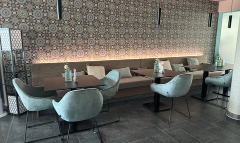 In einem modernen Café stehen runde Tische mit gemütlichen, geschwungenen Stühlen, umgeben von einem dekorativen Wandmuster.