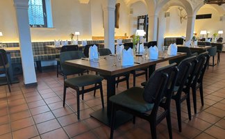 In einem hell erleuchteten Restaurant mit Holztischen und eleganten Stühlen sind Tischdecken und Gläser sorgfältig gedeckt.