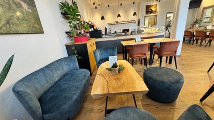 Der Innenraum eines einladenden Cafés mit stilvollen blauen Sitzgelegenheiten, einer rustikalen Holztisch und dekorativen Pflanzen.