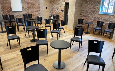Theatersaal mit mehreren schwarzen Holzstühlen und Säulentischen