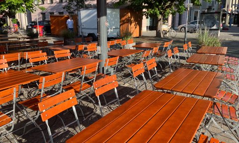 Weitläufige Freifläche mit Biergartentischen und -stühlen unter beschattenden Sonnenschirmen im Herzen von Ingolstadt.