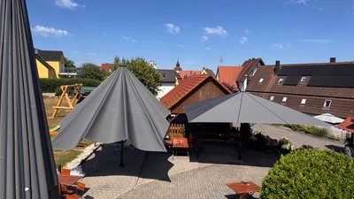 Der Außenbereich eines Gasthofs, ausgestattet mit modernen Sonnenschirmen und rustikalen Holzmöbeln, umgeben von ländlicher Idylle.