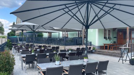 Ein einladender Außenbereich eines Restaurants mit großen Sonnenschirmen, Tischen und Stühlen auf einem hellen Pflasterboden.