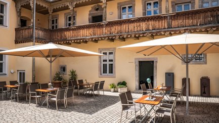 Ein gemütlicher Innenhof mit Tischen und Stühlen unter großen Sonnenschirmen, umgeben von historischen Gebäuden.