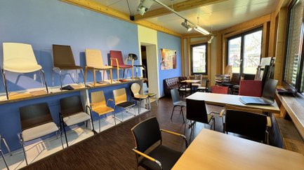 In einem hellen Ausstellungsraum sind mehrere Stühle und ein Tisch angeordnet.