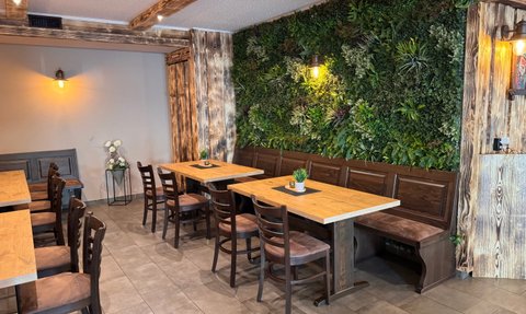 Der Raum zeigt rustikale Holzmöbel und eine grüne Wand aus Pflanzen, die eine einladende Atmosphäre schaffen.