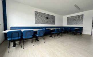 Die Einrichtung umfasst elegante blaue Stühle und Tische aus hellem Holz, ideal für geselliges Beisammensein.