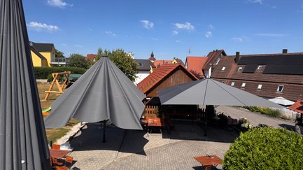Der Außenbereich eines Gasthofs, ausgestattet mit modernen Sonnenschirmen und rustikalen Holzmöbeln, umgeben von ländlicher Idylle.