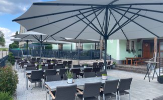 Ein einladender Außenbereich eines Restaurants mit großen Sonnenschirmen, Tischen und Stühlen auf einem hellen Pflasterboden.