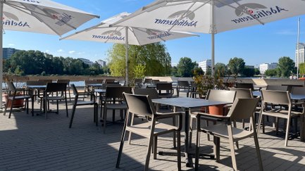 Modern gestalteter Cafébereich am Wasser, abgedeckt mit großen Sonnenschirmen und zahlreichen Tischen und Stühlen.