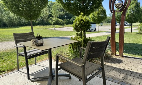 Ein sonniger Außenbereich mit mehreren Tischen und Stühlen, die auf eine entspannte Atmosphäre hinweisen.