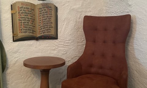 Der Sessel bietet einen einladenden Platz, während ein hängendes Licht und ein dekoratives Buch Atmosphäre schaffen.