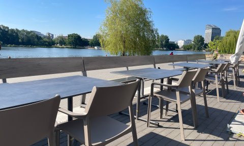 Modern gestalteter Cafébereich am Wasser, abgedeckt mit großen Sonnenschirmen und zahlreichen Tischen und Stühlen.