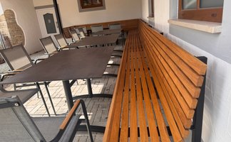In einem gemütlichen Gartenbereich sind eine Holzbank und mehrere Stühle um einen großen Tisch angeordnet, bereit für Gäste.