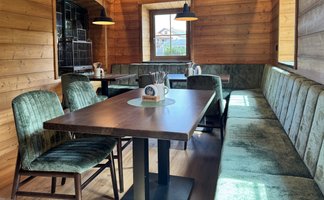 Der Innenraum eines rustikalen Restaurants mit Holzdecke, eleganten Lampen und einer einladenden Sitzbank aus Samt.