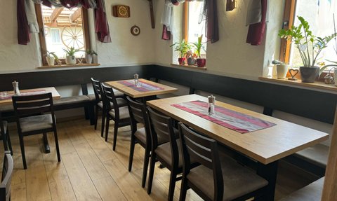 Der Innenraum eines gemütlichen Restaurants zeigt Holztische, Stühle und eine gemütliche Sitzbank.