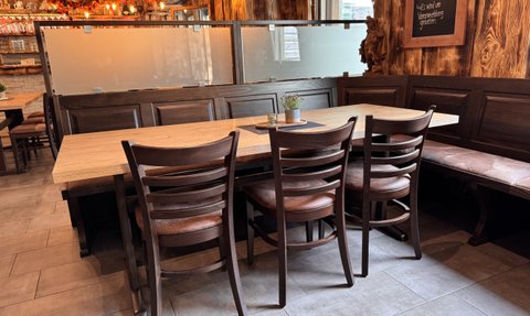 Einladende Tische mit Stühlen in einem gemütlichen Restaurant, umgeben von rustikalen Holzwänden und sanfter Beleuchtung.