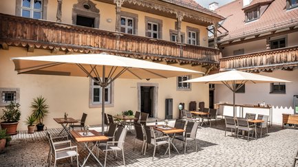 Ein gemütlicher Innenhof mit Tischen und Stühlen unter großen Sonnenschirmen, umgeben von historischen Gebäuden.