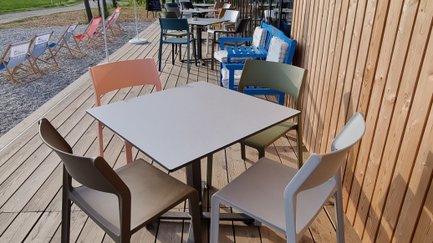 Auf der Terrasse des Cafés warten bunte Stühle und Tische auf Gäste, die die entspannte Atmosphäre im Freien genießen möchten.