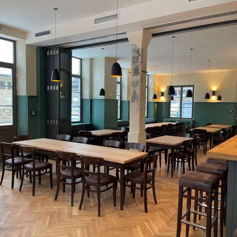 Helles, klassisches Restaurant mit Holzstühlen und großen Fenstern, das eine einladende Atmosphäre schafft.