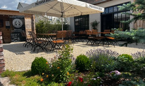 Ein gemütlicher Biergarten mit rustikalen Holzmöbeln und Sonnenschirmen bietet Platz für zahlreiche Gäste.