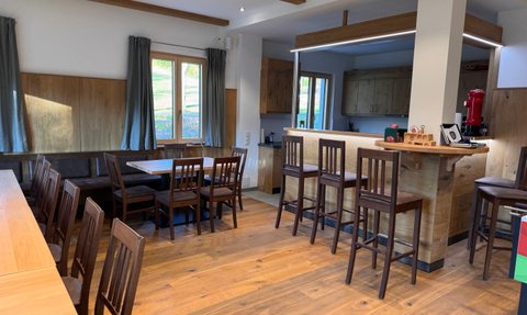 Ein einladender Gemeinschaftsraum mit Holzdetails, eleganten Stühlen und einem modernen Barbereich im Hintergrund.