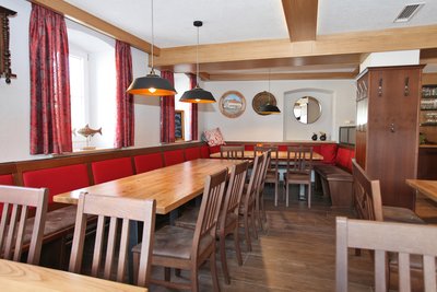 Holzeckbank mit rotem Lehnenpolster in Gastraum mit Holztischen und Holzstühlen