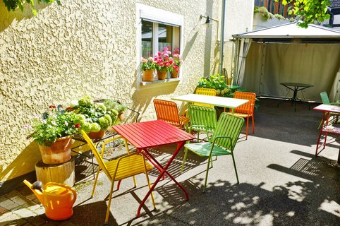 Zwei Tische mit mehreren bunt angestrichenen Stühlen in einem sonnigen Ambiente