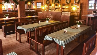 Wirtshausstuben mit dunkelbraunen Massivholzbänken und Stühlen und blau-weißen Tischdecken