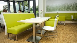 Grüne Sitzbänke und weiße Tische sowie Stühle in einer Sitzecke