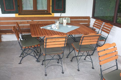 Eine Biergartengarnitur mit sechs Hlzstühlen, einer Bank und einem länglichen Tisch, allesamt aus Holz und Metallbeinen.