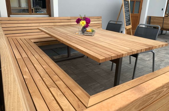 Um drei Ecken gehende Holzbank aus Robinienholz sowie ein Holztisch.