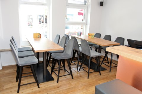 Sitzbereich mit grauen Schalenstühlen und holzfarbenen Tischen