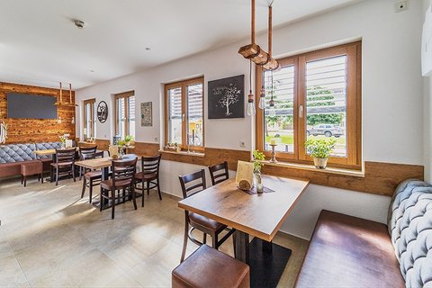 Sonnendurchfluteter Gastraum in einem Café mit drei Tischen und jeweils vier Stühlen sowie zwei Bänken
