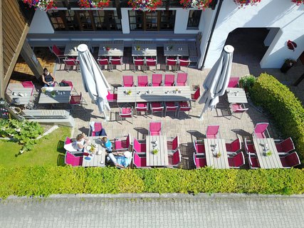 Drohnen-Sicht auf eine Terrasse mit Kunstgeflecht-Stühlen, Holztischen und zwei Schirmen