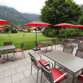 Außenbestuhlung für Biergarten mit rotgepolsterten Stühlen, Tischen und roten Schirmen